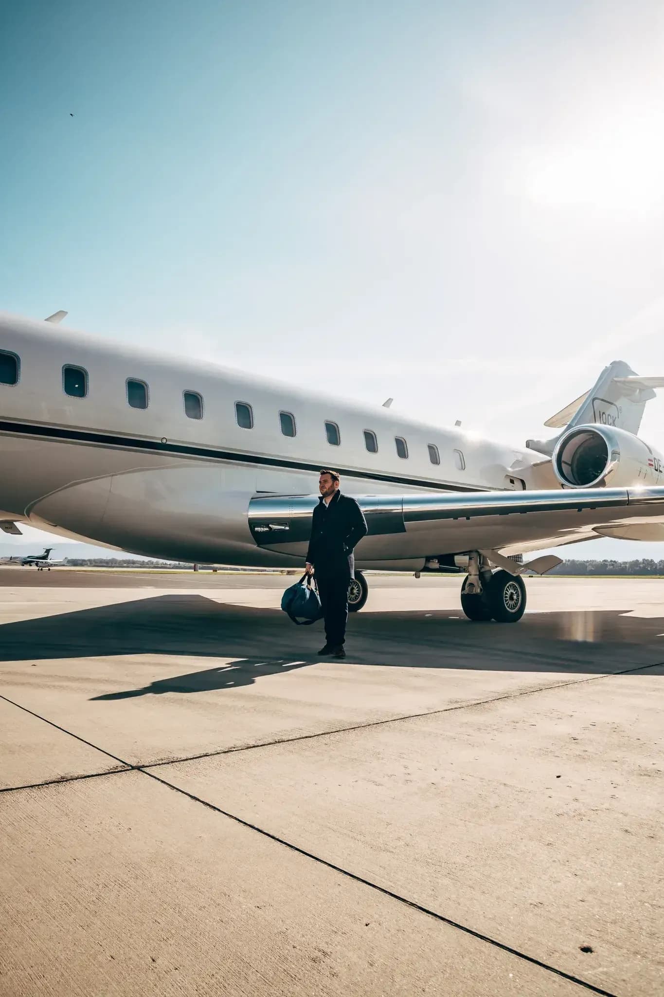 Zakenman met reistas die van een privéjet stapt op een zonovergoten tarmac.